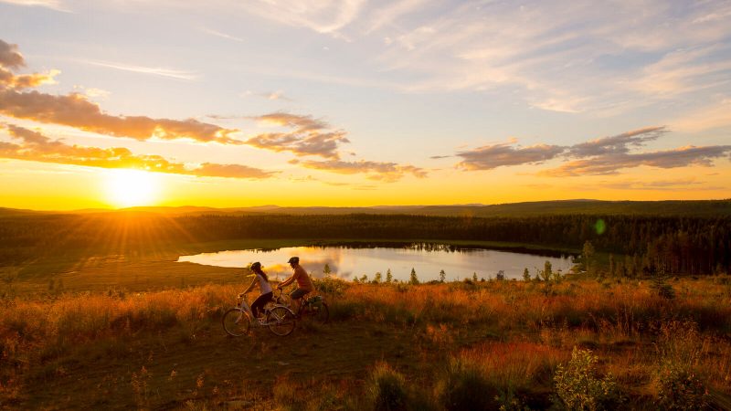Par som cyklar i solnedgång vid en sjö