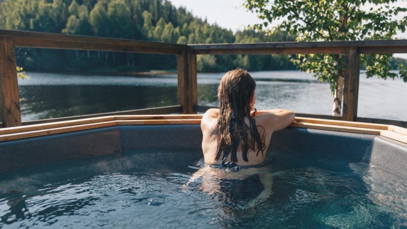 En kvinna sitter i en bubbelpool utomhus vid älven på sommaren.
